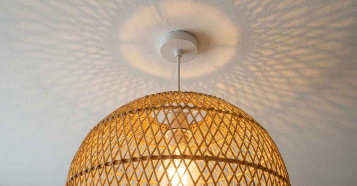 Rattan ball pendant shade fitted over a standard rental kitchen ceiling pendant cord, warm 2700K bulb glowing through the woven weave and casting a dappled shadow pattern on the ceiling